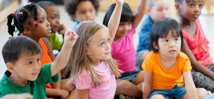 Library Hosts Preschool & Kindergarten Open House Classroom with students sitting on the floor and raising hands