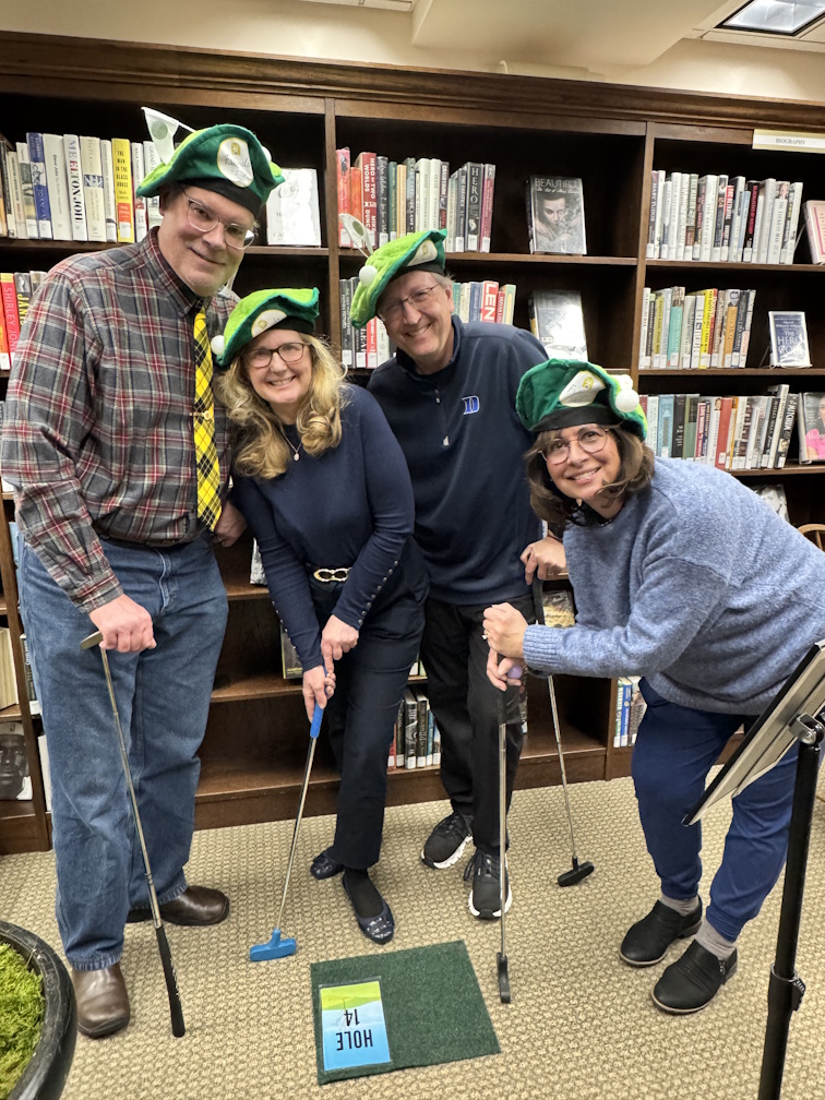 Four adults gathered around a putting green wearing matching golf-themed hats