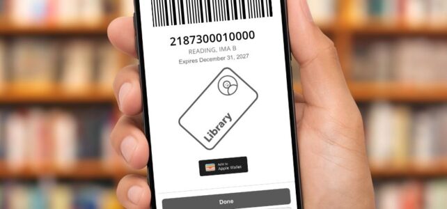 Hand holding phone featuring library app in front of blurred book shelves