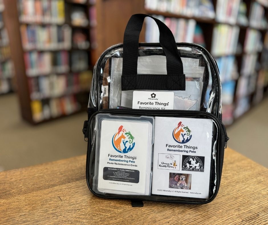 Clear plastic zip pouch with a black handle on a library table filled with booklets and cards.